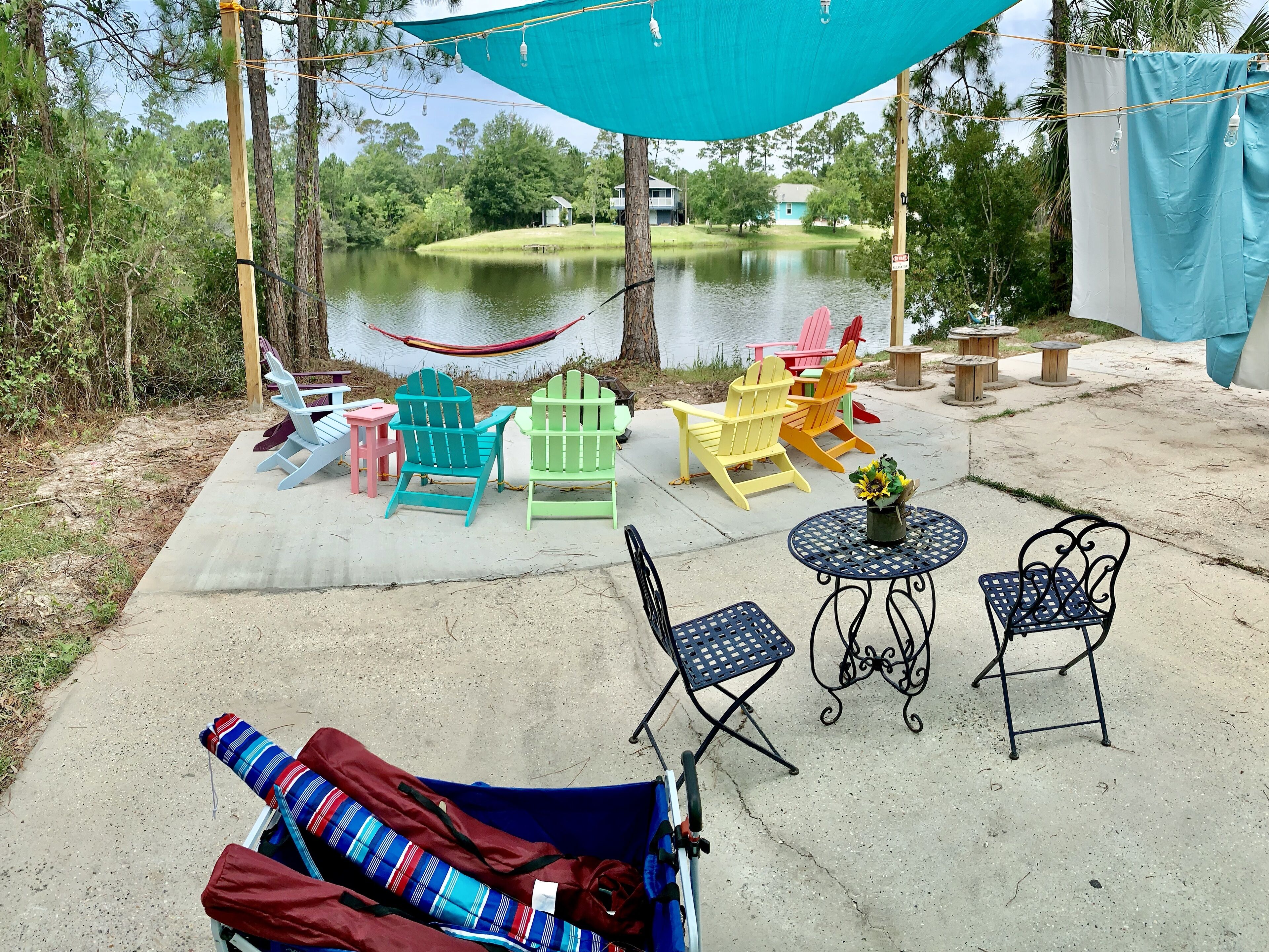Un espace patio agrémenté de chaises Adirondack aux couleurs vives, d’un hamac et d’une petite table ronde sur laquelle est posé un vase de fleurs.