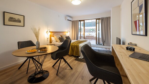 A modern hotel room with a wooden dining table, black chairs, a bed with a white duvet, and a large window with curtains. - The Apolo Loft in Downtown by Florit Flats (Valencia)