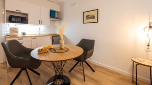 A modern kitchen with white cabinets, a microwave, and a sink. There is a dining table with two chairs and a vase with dried flowers. A framed picture is on the wall. - The Apolo Loft in Downtown by Florit Flats (Valencia)