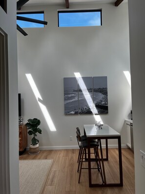 Un espace de repas moderne avec une table et des chaises en bois, une plante en pot et une grande œuvre d’art accrochée au mur.