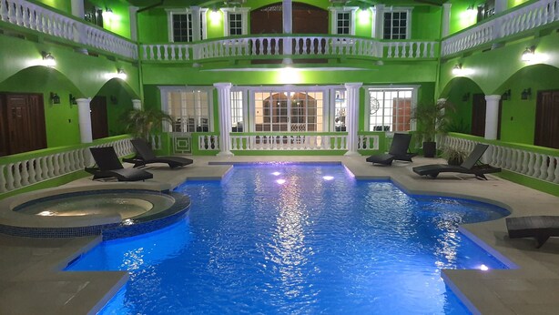 A large indoor swimming pool with a hot tub, surrounded by lounge chairs and a two-story building with balconies.