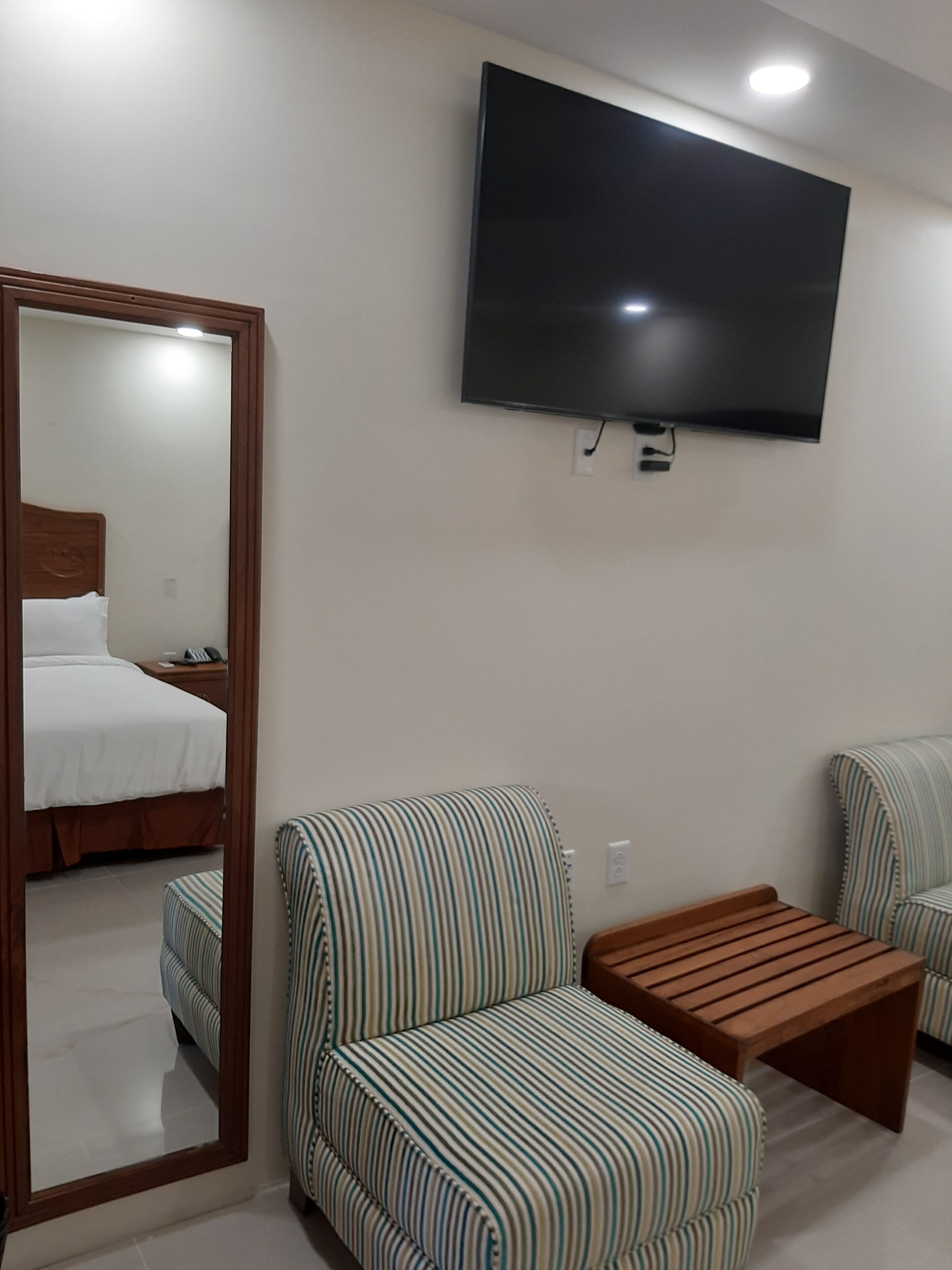 Une chambre d’hôtel avec un lit, un téléviseur fixé au mur et deux fauteuils à rayures.