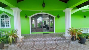 A bright green exterior with a patterned tile floor, white columns, and potted plants.