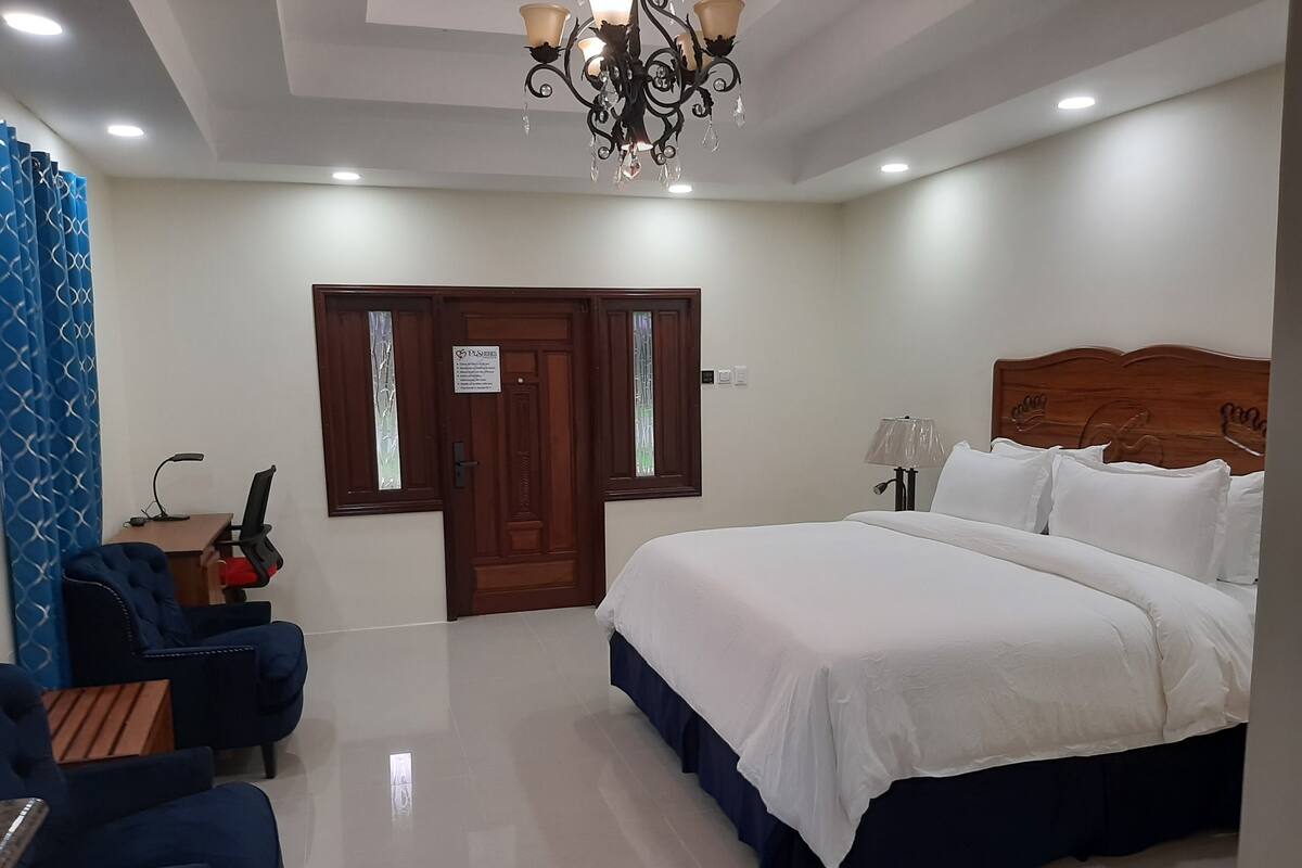A hotel room with a large bed, a desk with a chair, a chandelier, and a door with a sign.