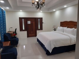 Habitación de hotel con una cama grande, un escritorio con silla, una araña y una puerta con un cartel.