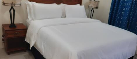 A neatly made bed with white linens, a wooden headboard, and two bedside lamps.