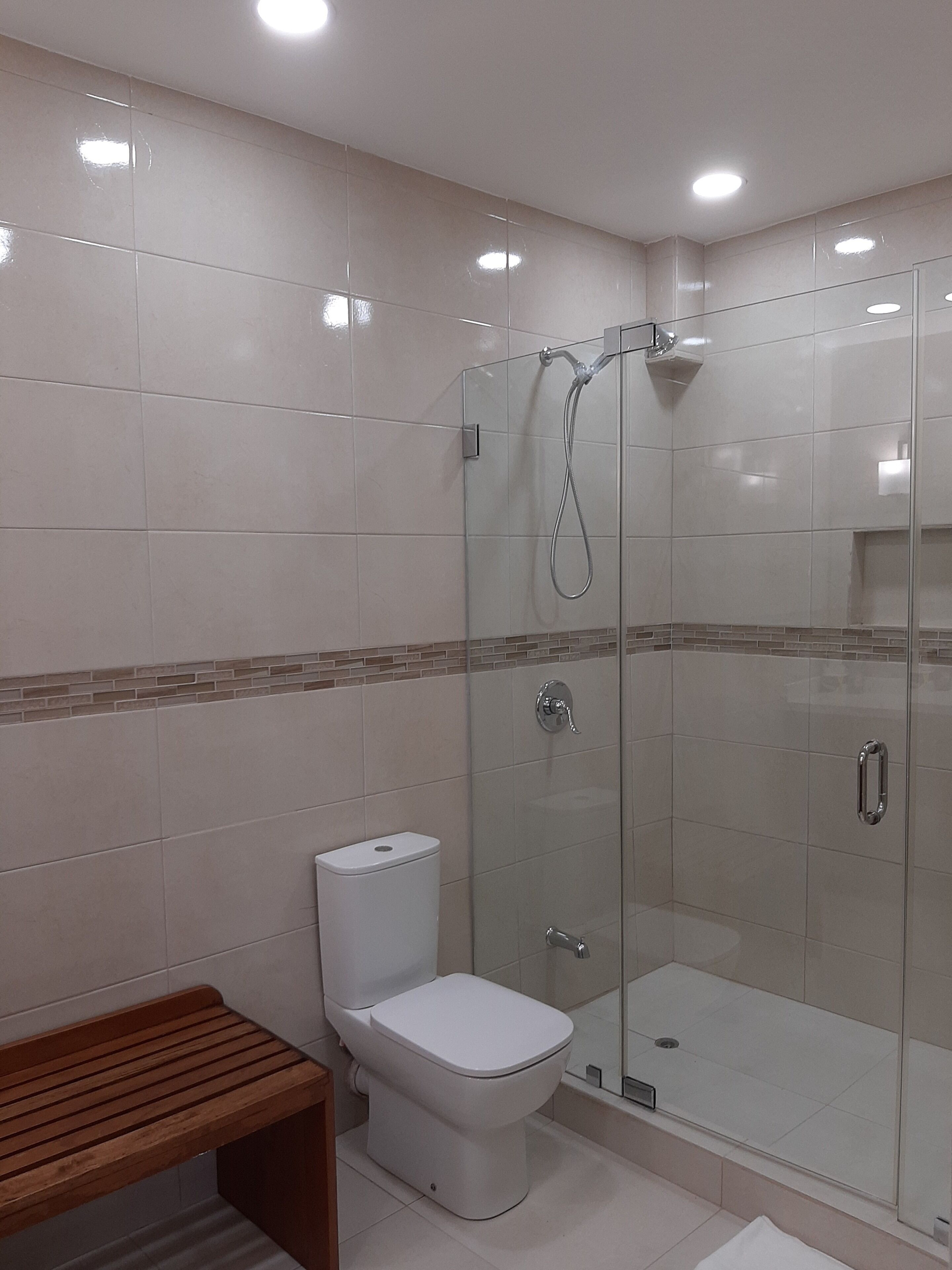 A modern bathroom with a glass-enclosed shower, a toilet, and a wooden bench.