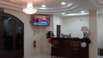 Un'area reception con un lampadario, una televisione che mostra 'Crime Watch' e una scrivania con sedie.
