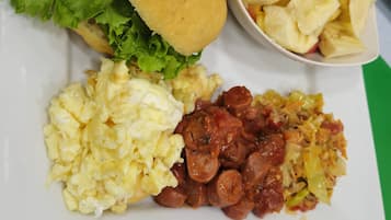 Un plato con huevos revueltos, salchicha, un sándwich y un tazón de chips de plátano.