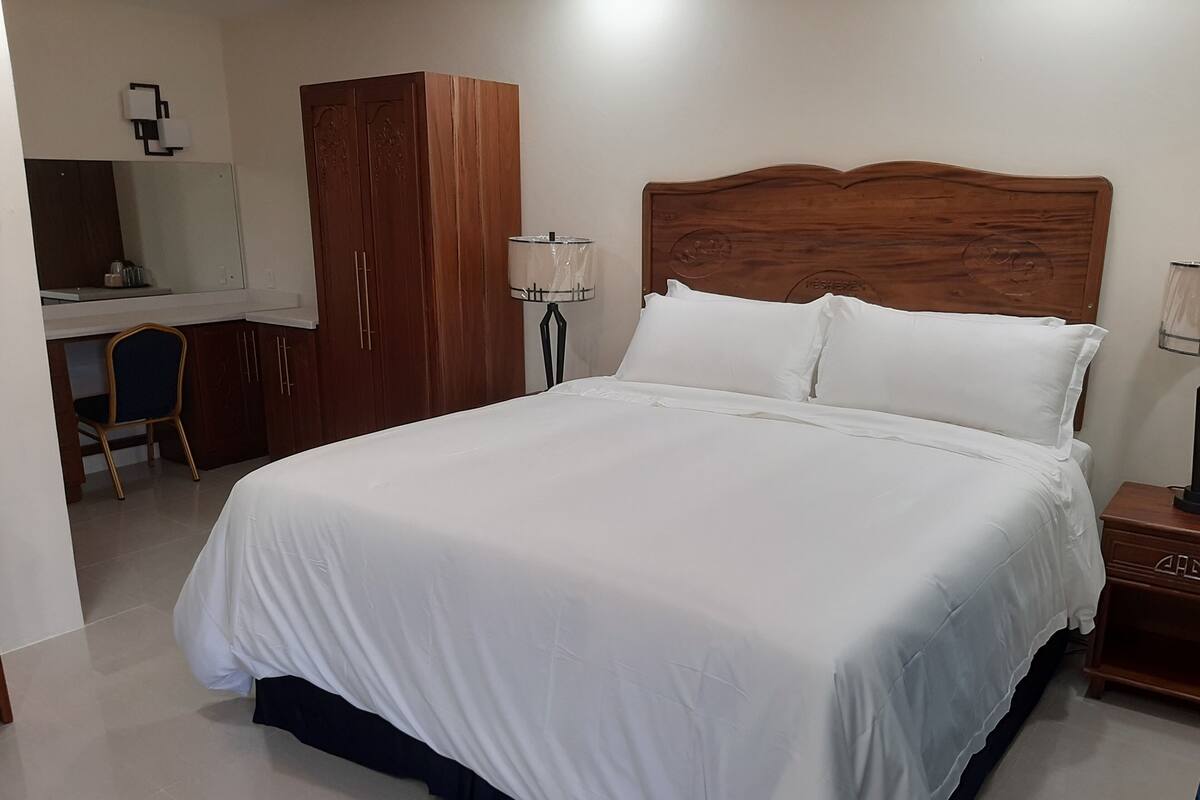 A neatly made bed with white linens, a wooden headboard, and a bedside table with a lamp.
