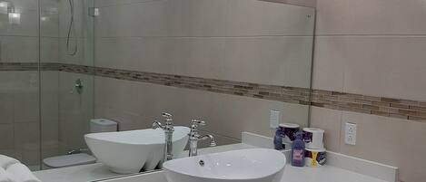 A bathroom with a large mirror, two sinks, a shower, and a towel rack.