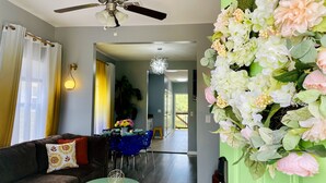 Ein Wohnzimmer mit einer Couch, einem Esstisch und Stühlen. Es gibt einen Deckenventilator, eine Kronleuchter und eine Wandleuchte.