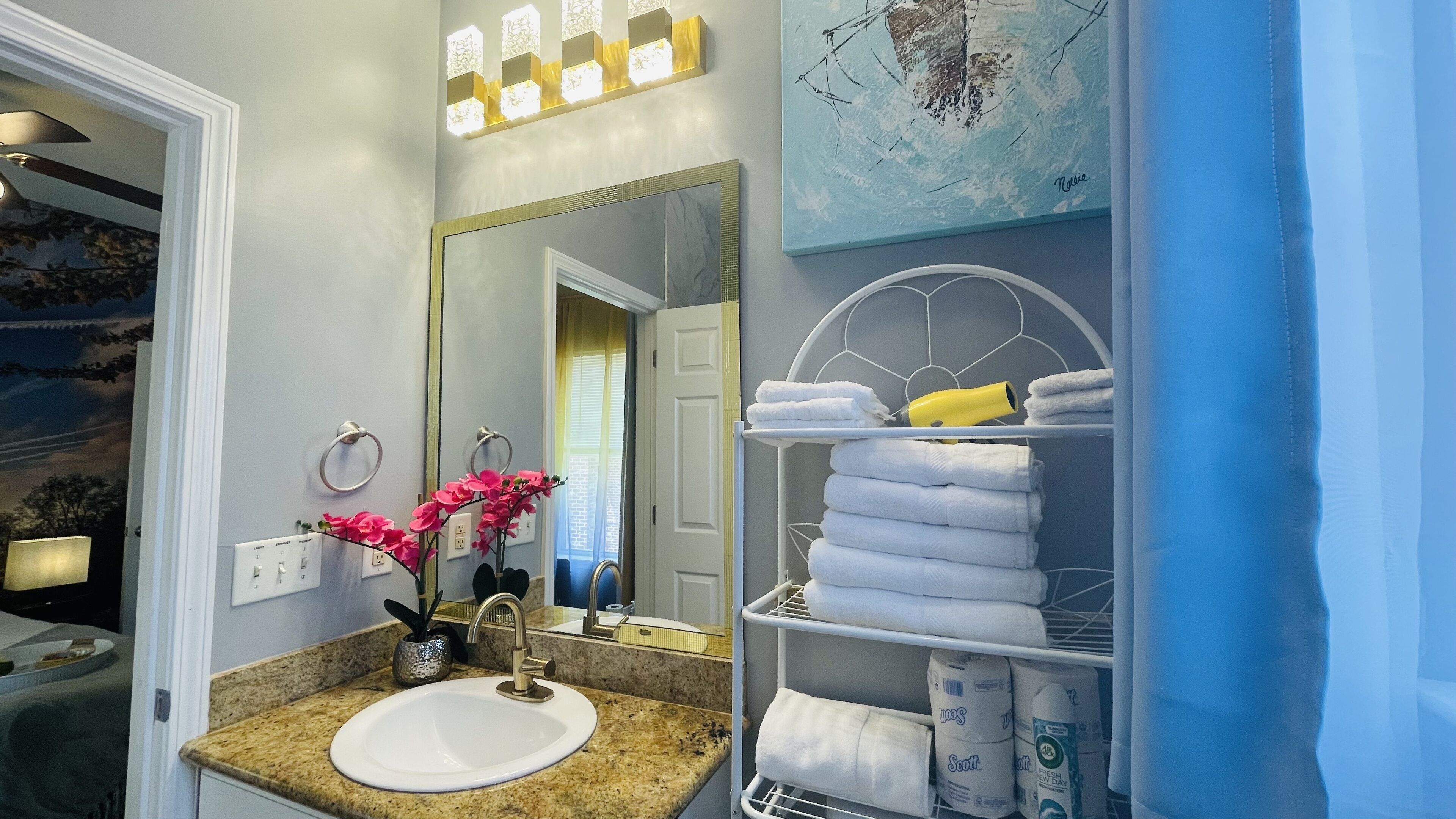A bathroom with a sink, mirror, towel rack, and shelves with towels and toiletries.