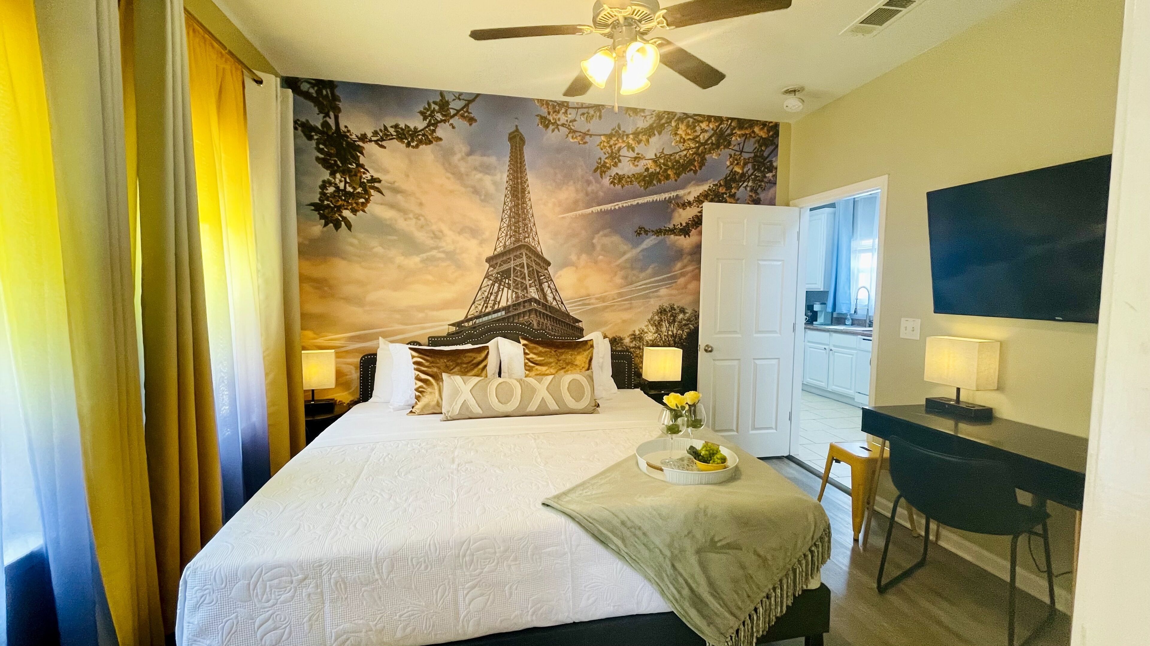 Une chambre d’hôtel équipée d’un lit, d’un bureau, d’une chaise, d’une télévision et ornée d’une fresque représentant la Tour Eiffel.
