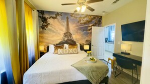 Ein Hotelzimmer mit einem Bett, einem Schreibtisch, einem Stuhl, einem Fernseher und einem Wandbild des Eiffelturms.