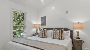 A bedroom with a bed, two bedside tables, a nightstand, a window with blinds, and a ceiling fan.