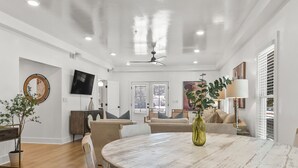 A spacious living area with a round table, sofas, and a television mounted on the wall.