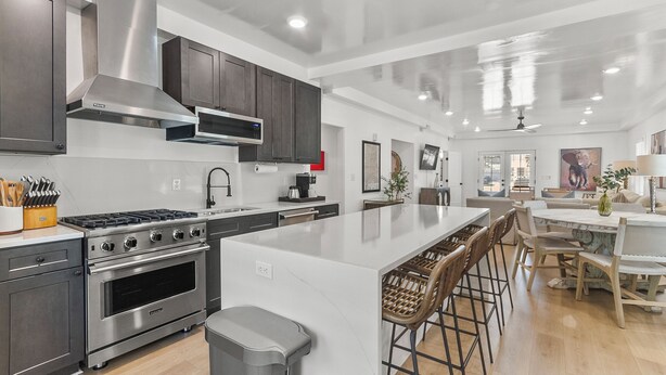 A modern kitchen with stainless steel appliances, a large island with bar stools, and a dining area with a white table and chairs.
