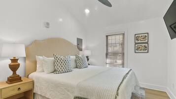 A bedroom with a bed, bedside tables, a ceiling fan, a window with blinds, and wall-mounted artwork.