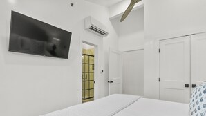 Ein Schlafzimmer mit einem Bett, einem an der Wand montierten Fernseher, einem Kleiderschrank und einer Tür zu einem anderen Raum.