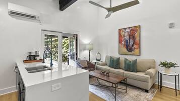 A modern kitchen with a central island, a dining area with a sofa and coffee table, and a living room with a couch and a painting.