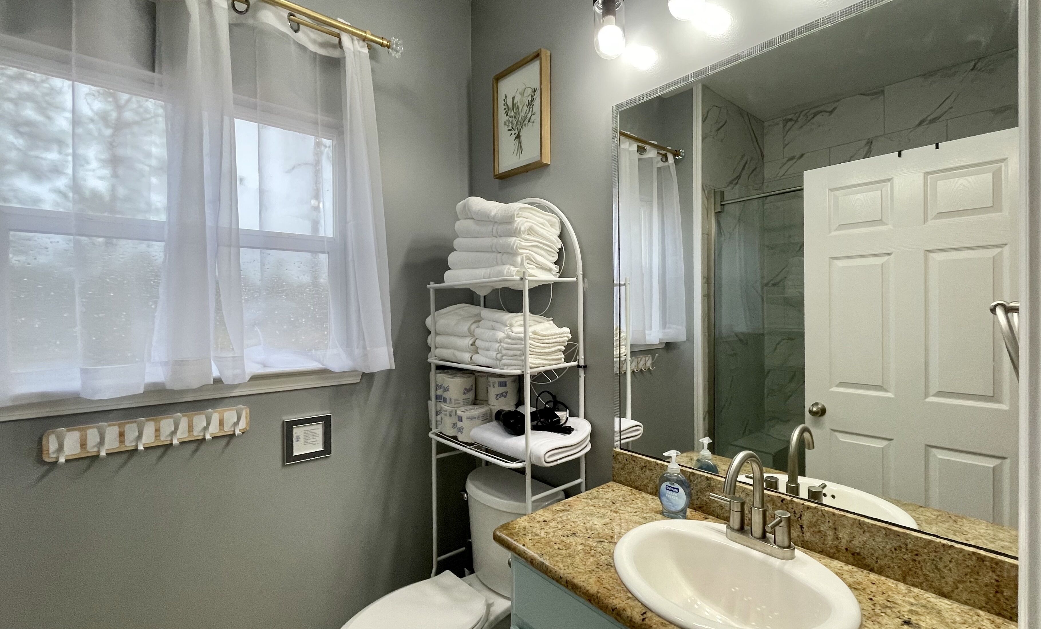 A bathroom with a sink, mirror, towel rack, and shower.