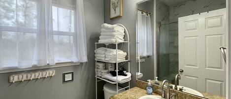 A bathroom with a sink, mirror, towel rack, and shower.