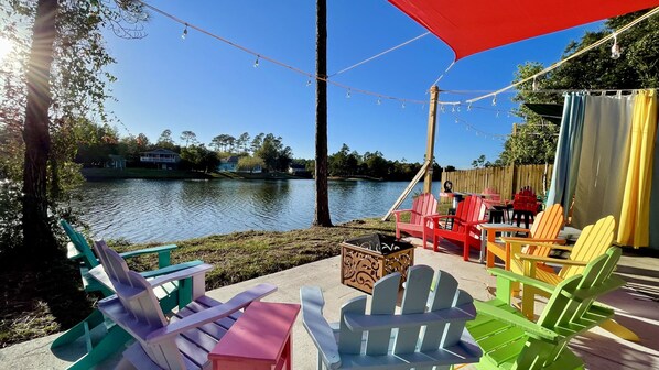 A lakeside patio with colorful Adirondack chairs, a table, and a red umbrella.