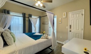 A bedroom with a bed, a bedside table, a chair, a door, and a ceiling fan.