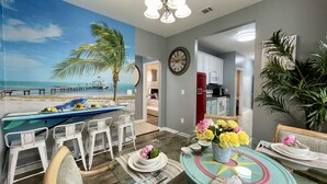 Un comedor con un mural de playa, un reloj y una cocina al fondo.