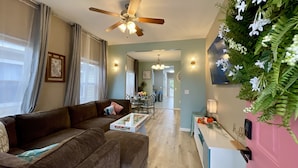 Ein Wohnzimmer mit braunem Sofa, einem Couchtisch, einem Deckenventilator und einem Essbereich mit Tisch und Stühlen.