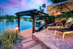 An outdoor patio with a pergola, seating area, and a view of a lake. - Lakefront Oasis: Pool, Hot Tub, Dock, Pedal Boat, Queen Bunk Room (Mesa)