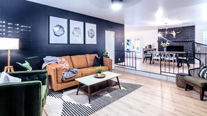 A modern living room with a dark wall, a brown sofa, a coffee table, and a dining area with a black fireplace. - Lake Front Paradise, Pool and Hot Tub-Bubbly (Mesa)