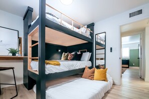 A bunk bed room with a desk and chair, a framed picture on the wall, and a plant on the desk.