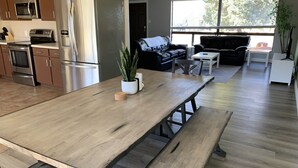 Eine moderne Küche mit Edelstahlgeräten, ein Essbereich mit Holztisch und Bänken sowie ein Wohnzimmer mit Sofa und Couchtisch.