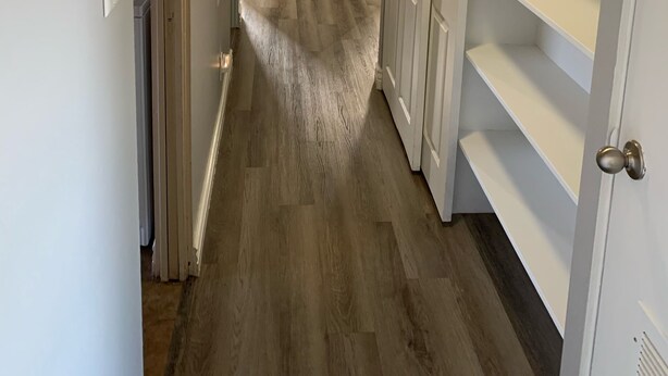 Ein schmaler Flur mit Holzboden, weißen Wänden und einem Einbauschrank mit Regalen.