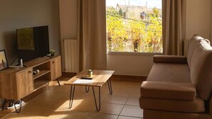 Una sala de estar con un sofá, un televisor sobre un mueble de madera, una mesa con un control remoto y una ventana con cortinas.