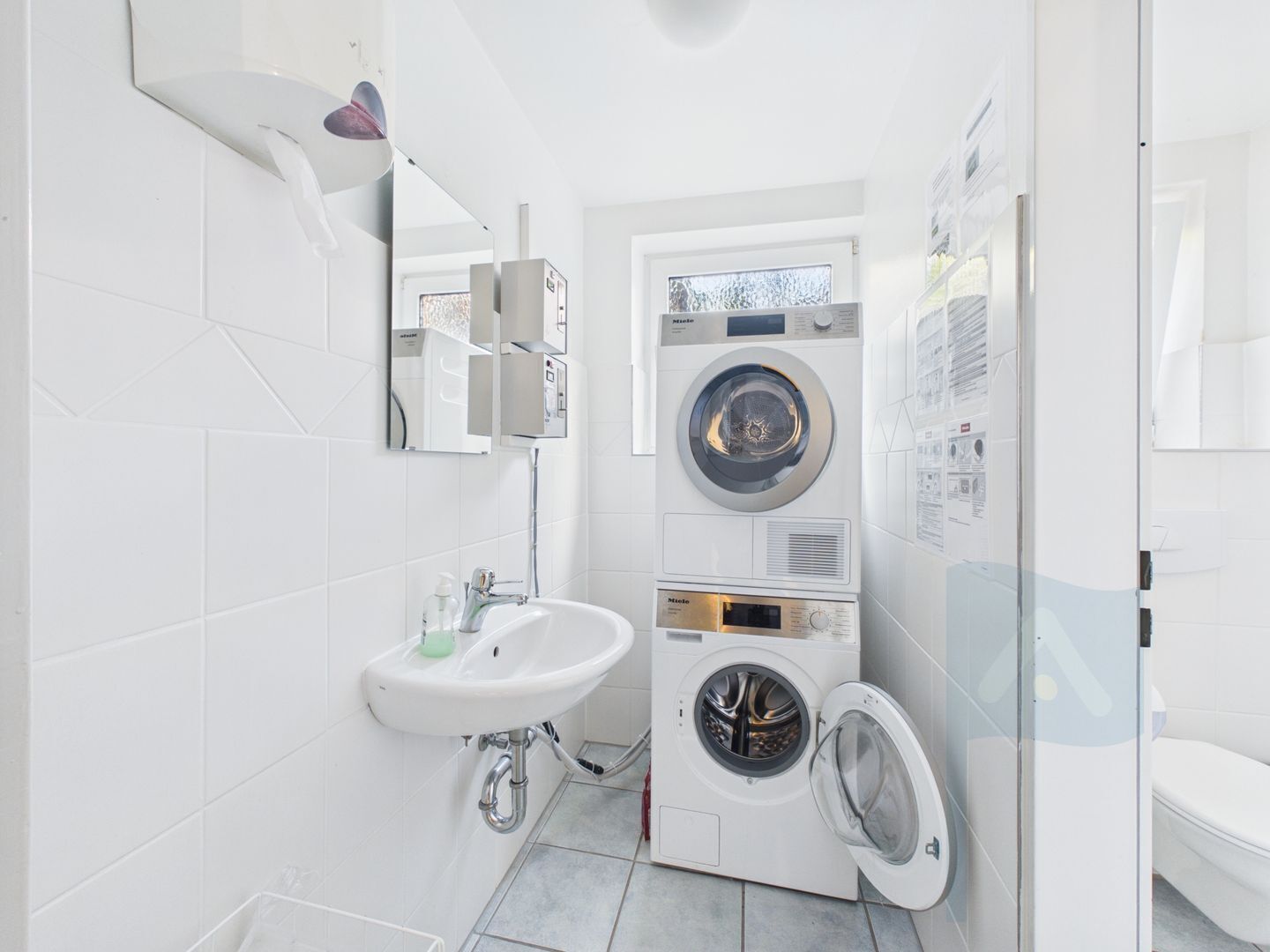 A compact bathroom with a sink, mirror, and stacked washer-dryer unit.
