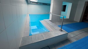 A swimming pool with a glass enclosure, a metal handrail, and a blue mat at the bottom.