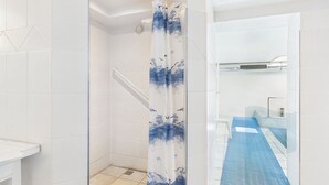 A modern bathroom with white tiles, a shower with a blue and white curtain, and a blue shower mat.