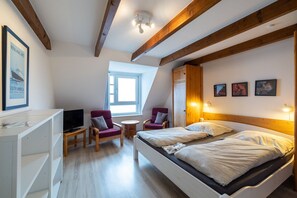 Een kamer met een bed, twee stoelen, een tafeltje, een televisie en een raam.