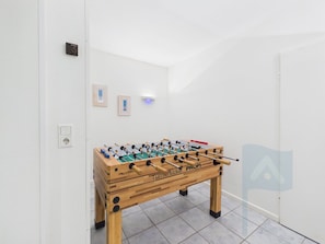 A room with a wooden foosball table, a wall socket, and two framed pictures.