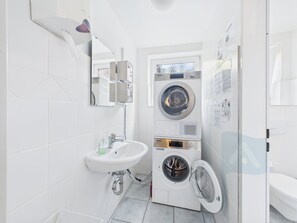 Een kleine badkamer met een wastafel, spiegel en een gestapelde wasmachine-droger combinatie.