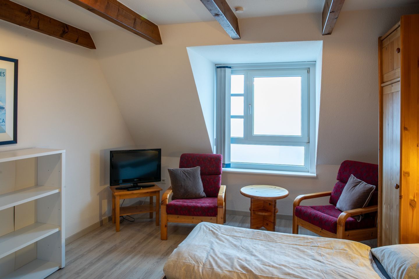 Ein Zimmer mit einem Bett, zwei Sesseln, einem kleinen Tisch, einem Fernseher und einem Fenster.