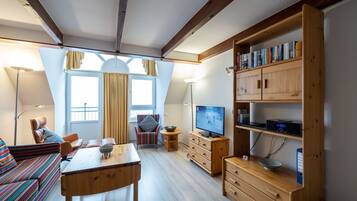 Ein gemütliches Wohnzimmer mit einer Couch, einem Fernseher, Holzschränken und einem Esstisch.