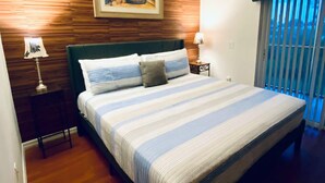 A bedroom with a wooden wall, a bed with striped bedding, a nightstand with a lamp, and a window with blinds. - Huge Screened Patio That Overlooks Lake Buck, Near Famous Attractions!! (Kissimmee)