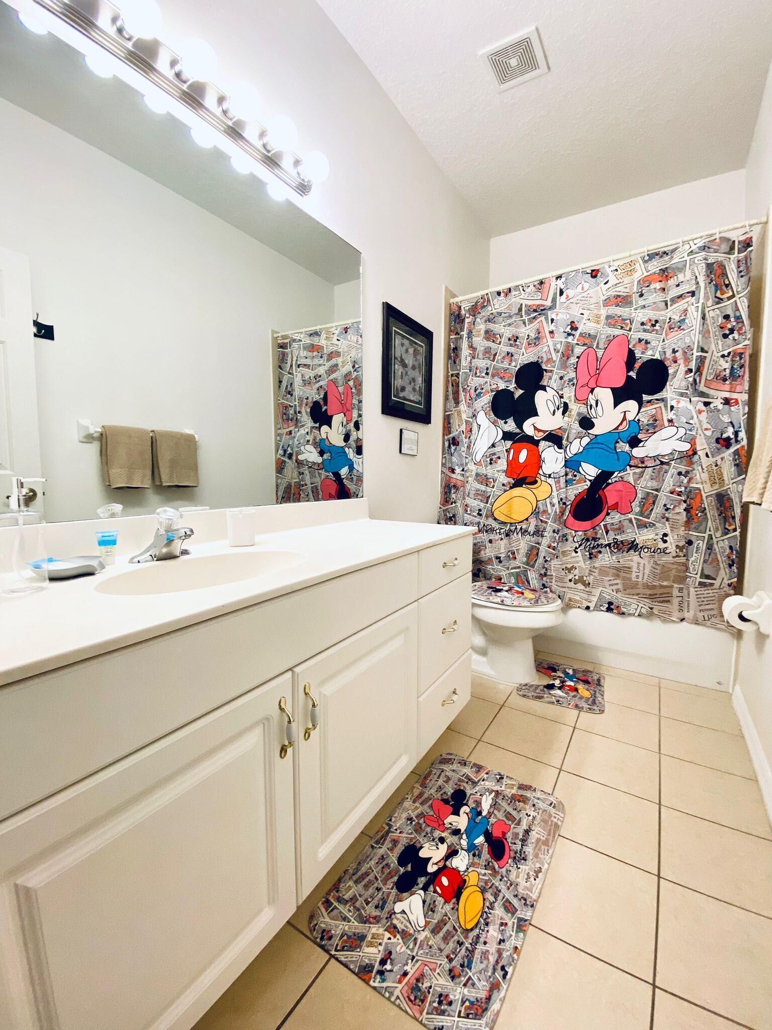 A bathroom with a Mickey Mouse themed shower curtain, a white sink, and a mirror with lights above it.
