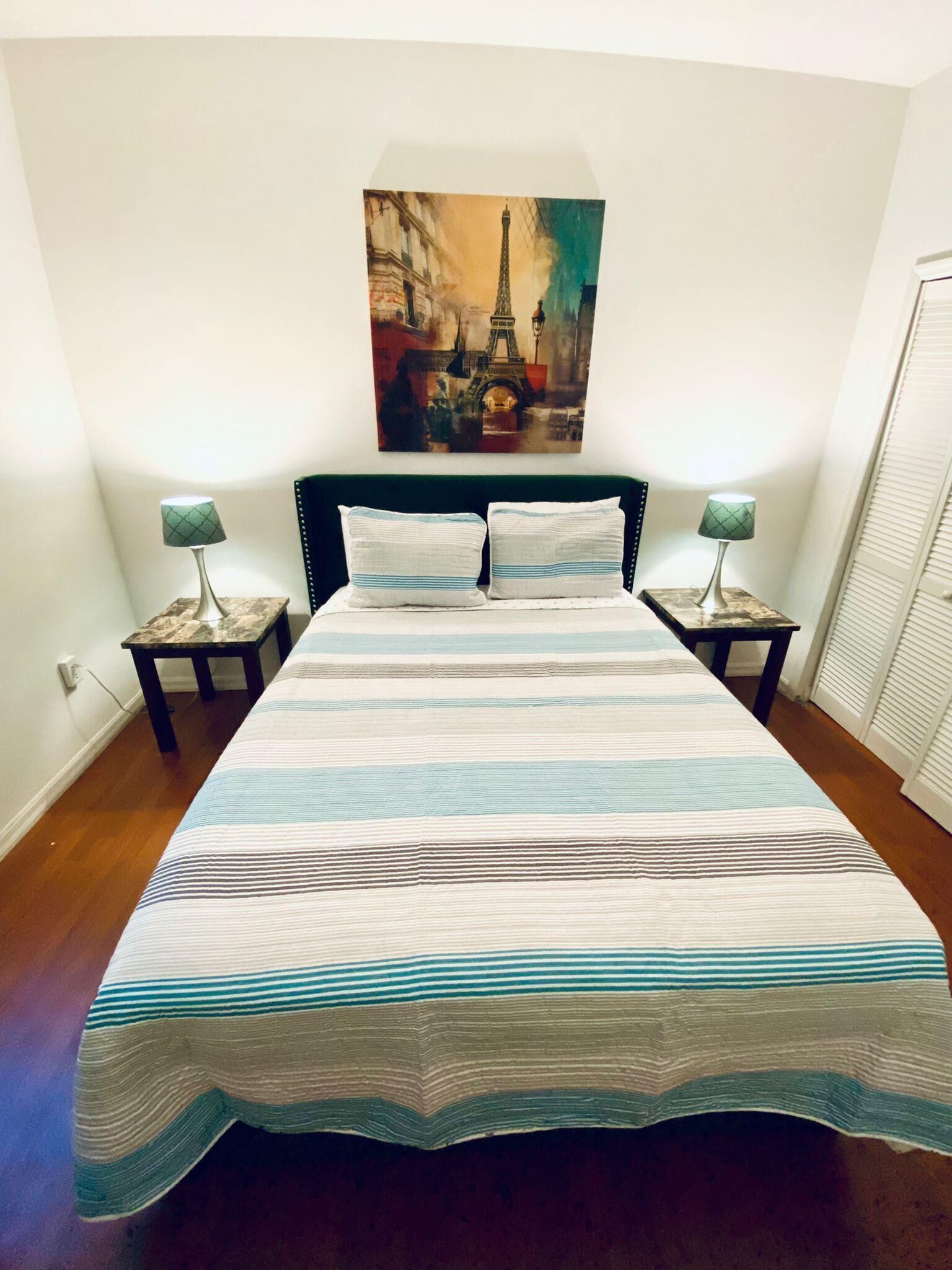 Una cama con colcha a rayas, dos almohadas y dos mesitas de noche con lámparas.