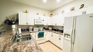 A kitchen with white cabinets, a granite countertop, a stainless steel sink, a microwave, a refrigerator, and decorative items on the cabinets. - Huge Screened Patio That Overlooks Lake Buck, Near Famous Attractions!! (Kissimmee)