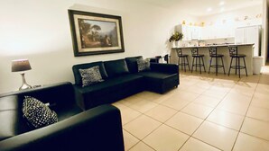 A modern living room with a black sofa, a dining area with bar stools, and a kitchen in the background. - Huge Screened Patio That Overlooks Lake Buck, Near Famous Attractions!! (Kissimmee)